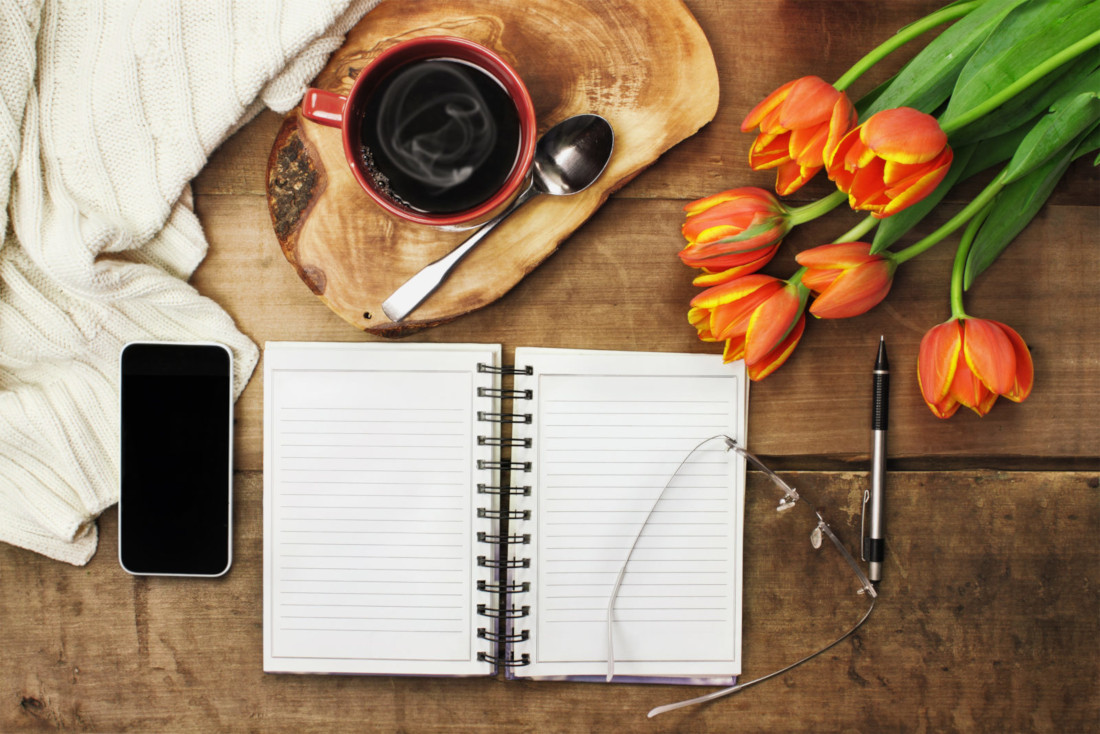 Open notebook with phone, coffee, and flowers on the table