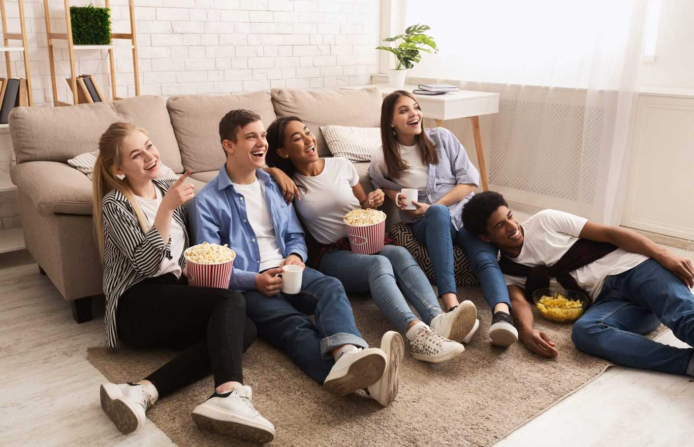 Happy friends watching comedy film at home and eating popcorn on floor