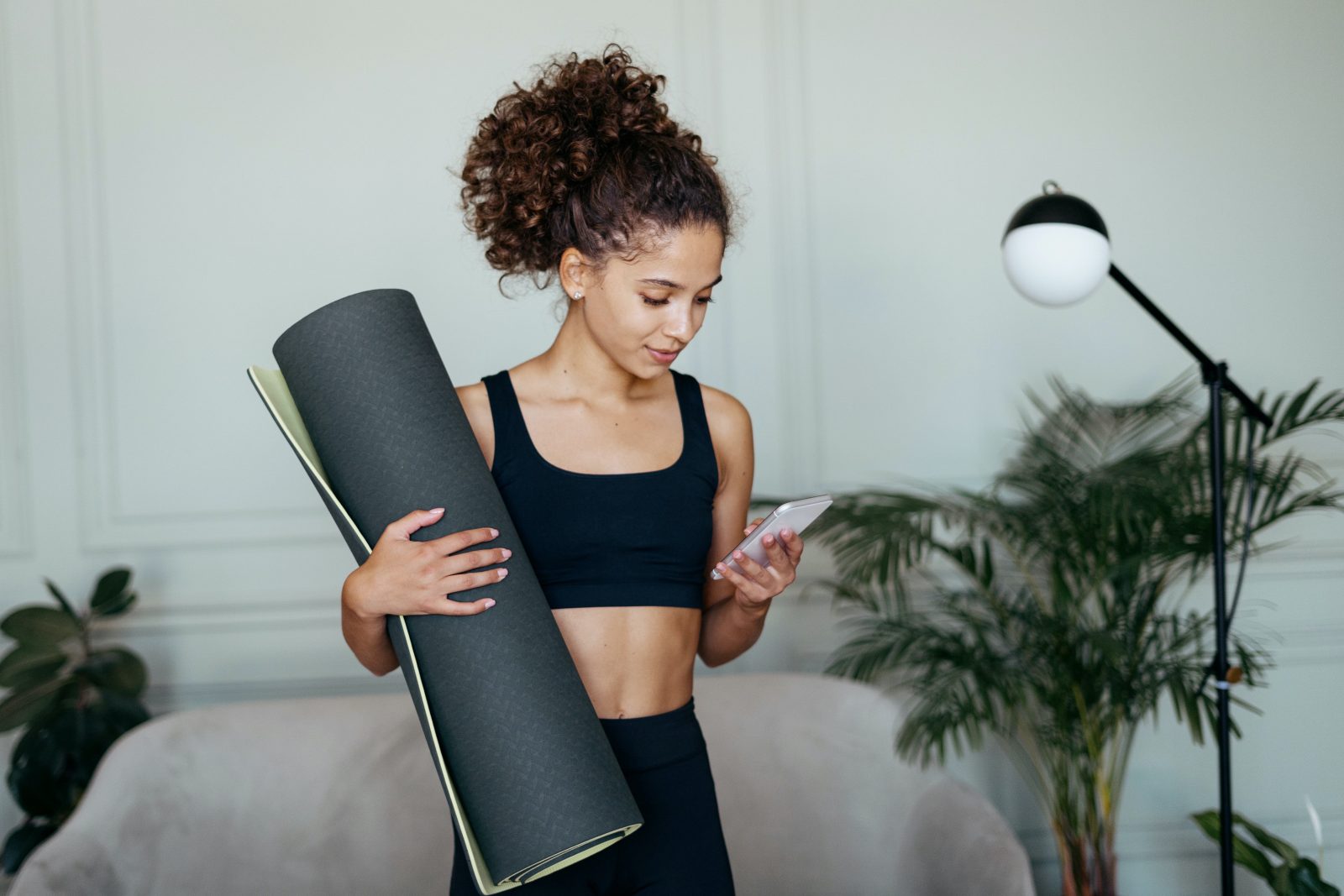 Sporty woman holds her yoga mat while looking at her smart phone in preparation of a workout.